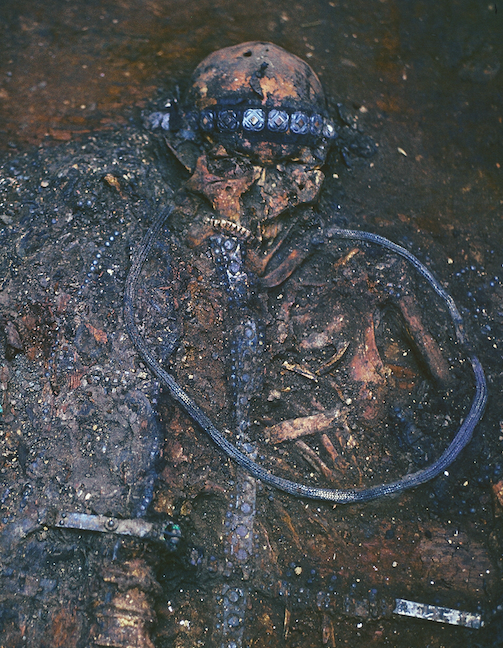 <p>Close view of the burial during the excavation, 1981. The electrum belt is put around the neck of the deceased as a sign of submission to gods. On the waist is one of Crusader belts. Also discernable compositions of embroidery and metal plaques, decorating the loros kaftan and the inner tunic. The photograph demonstrates impressively meticulous work of the archeologists. (source: V. I. Klochko)</p>